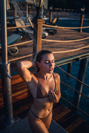 Beautiful young woman takes a relaxing shower in a swimsuit on a sunny day outdoors by the sea. The girl on vacation is resting. Selective focusの写真素材