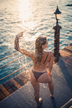 Beautiful young woman takes a relaxing shower in a swimsuit on a sunny day outdoors by the sea. The girl on vacation is resting. Selective focusの写真素材
