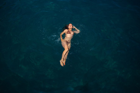 A beautiful young attractive woman in a swimsuit lies on the surface of the water at the sea. View from above. She is enjoying her vacation. Selective focusの写真素材