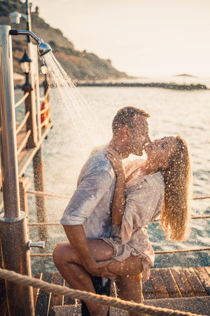 Happy couple by the sea. A guy and a girl are under the shower on an open-air pier. Happy couple on vacation. Man and woman by the sea.の写真素材
