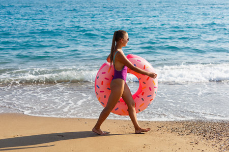Woman on the beach walks with an inflatable ring in the sea, walks relaxing in a tropical paradise for relaxation. Young model sunbathing on summer vacation.の写真素材