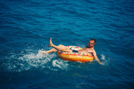 A young man swims in the open sea on an inflatable ring on a sunny day. Summer vacation, tourist on...