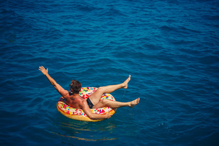 A young man swims in the open sea on an inflatable ring on a sunny day. Summer vacation, tourist on...
