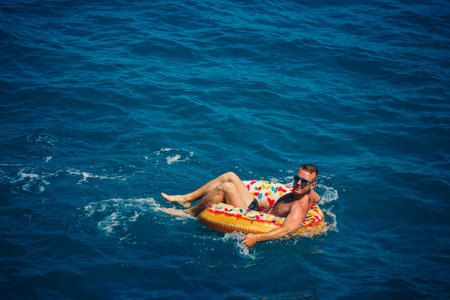 A young man swims in the open sea on an inflatable ring on a sunny day. Summer vacation, tourist on...