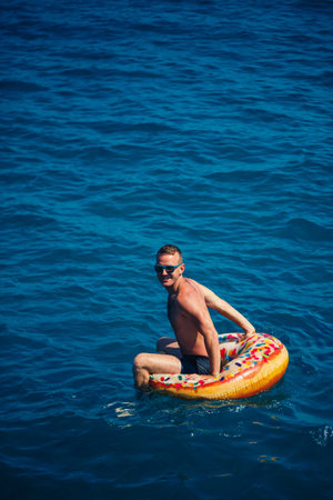 A young man swims in the open sea on an inflatable ring on a sunny day. Summer vacation, tourist on vacationの写真素材