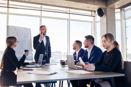 Confident businessman makes a presentation of a new project in the boardroom at a company meeting. Beautiful auditors talk with different partners about the business using a whiteboard and graphs.の写真素材