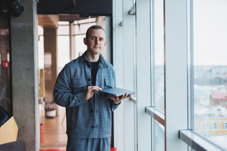Portrait of a smart intelligent male manager, he is holding a laptop for research in the office, a...