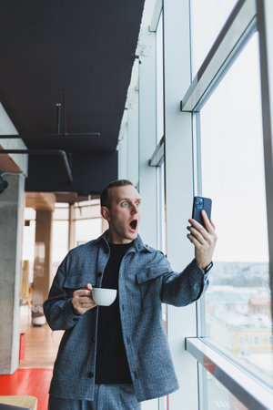 Excited young man in suit using mobile phone with funny expression, excited business man looking at his smartphone, reading good news via email, emotional lifestyle concept.の写真素材