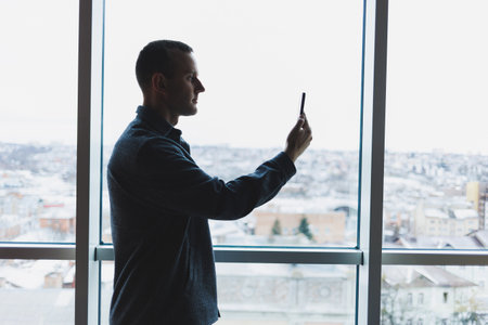 Young business man holding a phone. In an office or business center against the background of large windows of a skyscraper. Work and career, conceptの写真素材