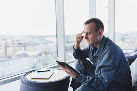 A male businessman in a casual suit resting in a comfortable pouf while working, an attractive...