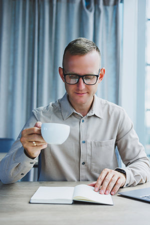 A freelancer in glasses works on a laptop and drinks coffee, a manager sits at a table in the...