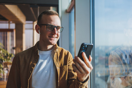 Modern office worker using smartphone app for service consultation in modern workspace, man talking on the phone. Remote work, male freelancerの写真素材
