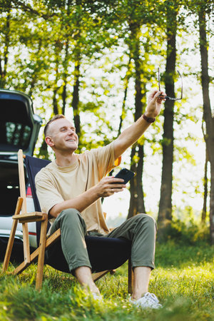 Freelancer man sits on a wooden chair in nature and works online on a laptop. A man travels and...
