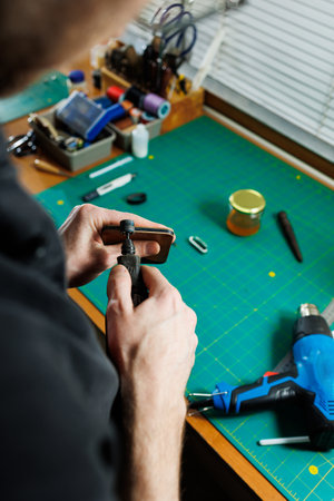 The hands of the master sew handmade leather products. Men's hands connect the parts, creating...