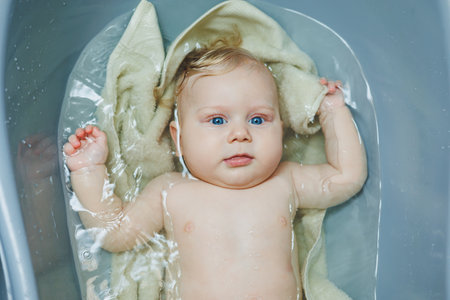 A small newborn boy of 5 months is bathing in a bathtub. Baby care.