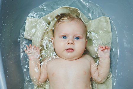 A small newborn boy of 5 months is bathing in a bathtub. Baby care.