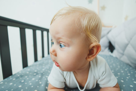 A small child is lying in a crib at home. Portrait of a five-month-old baby lying in a playpen....