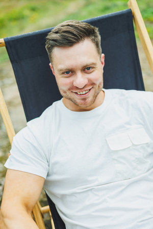 A man sits on a folding wooden chair in nature and rests. The concept of recreation in nature alone.の写真素材