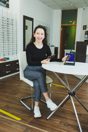 A young woman sits and chooses glasses in an ophthalmology salon. Bad eyesight.の写真素材