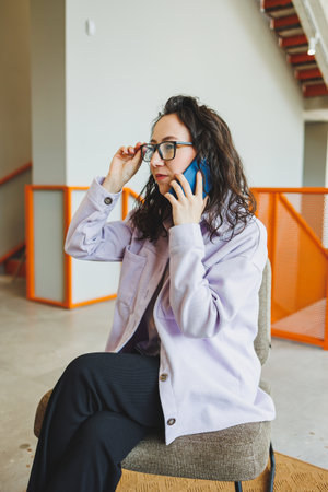 Emotional pretty woman in glasses in casual clothes sitting in comfortable chair in modern cafe at...