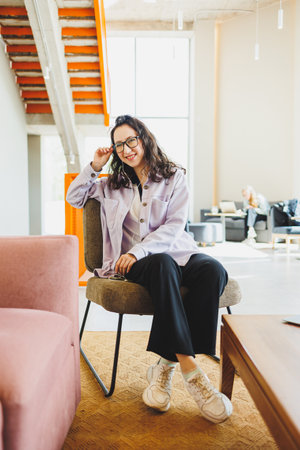 A stylish woman in glasses sitting in a modern cafe at a table with a phone works online. A woman is...