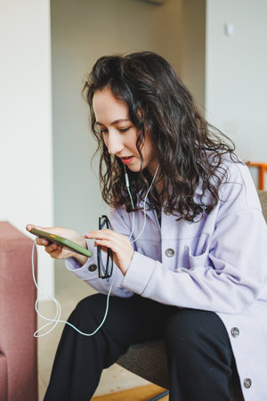 A stylish woman in glasses sitting in a modern cafe at a table with a phone works online. A woman is...