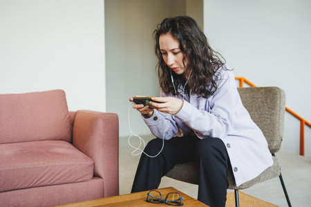 A stylish woman in glasses sitting in a modern cafe at a table with a phone works online. A woman is...