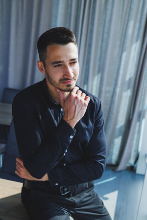 Young successful male worker in glasses and black shirt sitting on desk and working on project via...