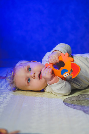 A 6-month-old child is lying on a mat and biting a rodent. A teether in the hands of a babyの写真素材
