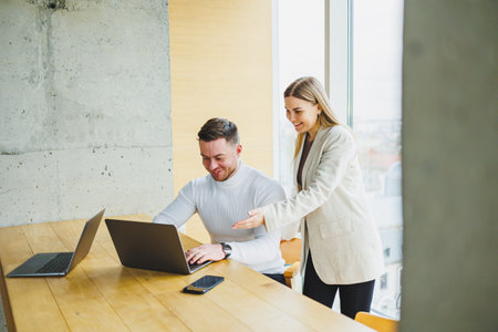Male and female colleagues are working at a wooden table on laptops and talking. Concept of business...