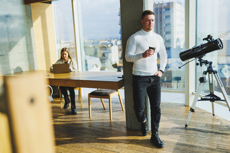 Cute young male freelancer drinking coffee while sitting in bright workspace working remotely. A man...