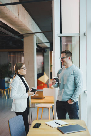 Business people man and woman over coffee discussing business looking at laptop, modern workspace. Colleagues work together in the officeの写真素材