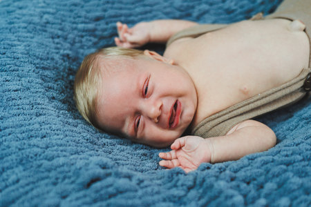 A 2-month-old baby is lying in knitted pants on a gray blanket. Clothes for babies