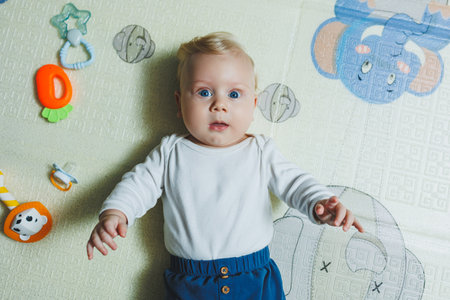 A 5-month-old baby is smiling and lying on a developmental mat. Self-development of the child.