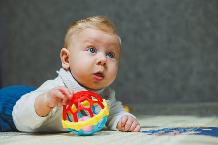 A four-month-old boy lies on the floor on a rug and plays with toys. The child holds his head. A...