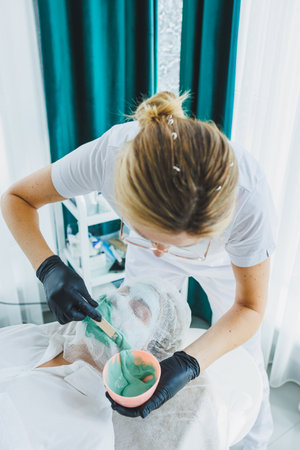 A woman is lying down at a dermatologist's appointment. Facial skin treatment. Applying a mask to a woman's faceの写真素材
