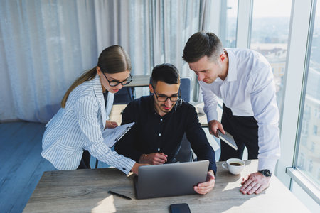A team of businessmen in formal wear discussing project details and looking at laptop screen while collaborating during a meeting in a modern boardroom. Modern officeの写真素材