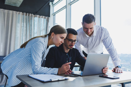 A team of businessmen in formal wear discussing project details and looking at laptop screen while collaborating during a meeting in a modern boardroom. Modern officeの写真素材