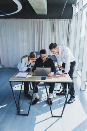 A team of businessmen in formal wear discussing project details and looking at laptop screen while collaborating during a meeting in a modern boardroom. Modern officeの写真素材
