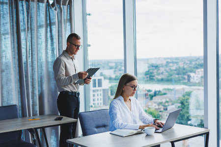 Smiling business woman sitting at a table with a laptop, keeping her back to her partner sitting at the desktop. The concept of successful teamwork.の写真素材
