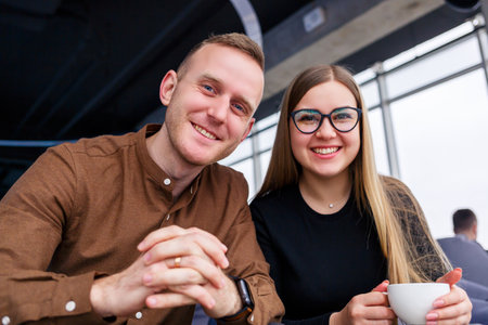 A successful young woman manager with her boss sits with a laptop on an upholstered armchair by the panoramic window and drinks coffee. Business woman and man working on a new projectの写真素材