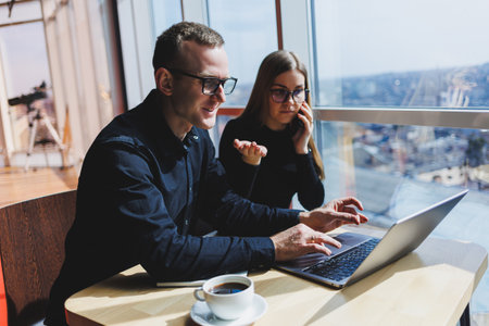 We work together on a business project. Two young business colleagues work on a laptop in a modern...