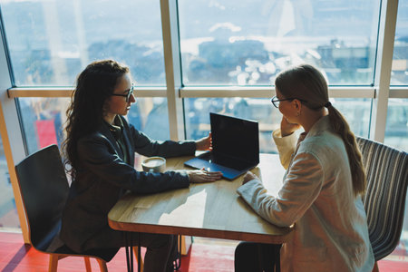 Two female co-workers and colleagues discussing working together on business project using laptop, female executive explaining new online idea to co-worker analyzing computeの写真素材