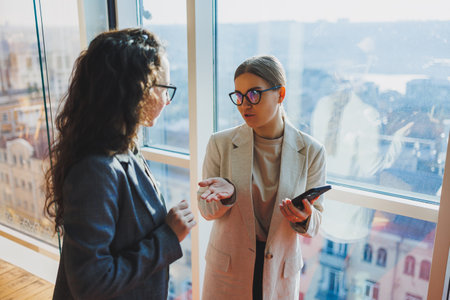 Top view of smiling young confident business workers in casual clothes standing on modern office background and talking during day breakの写真素材