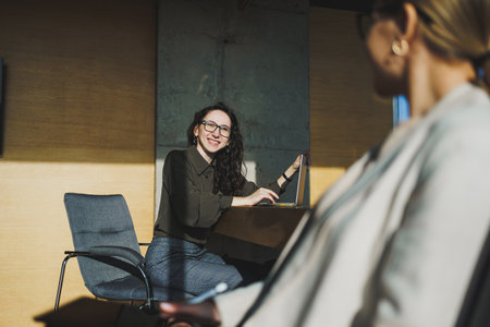 Smiling positive diverse colleagues in casual clothes working on a new project sitting together at the negotiation table during a meeting in a bright creative workspaceの写真素材