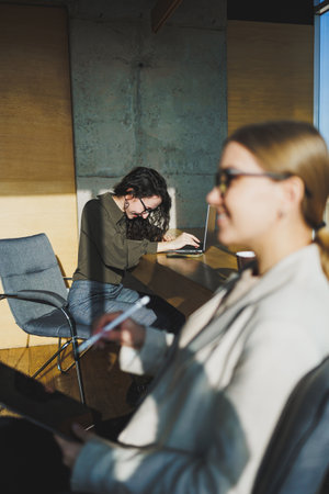 Smiling positive diverse colleagues in casual clothes working on a new project sitting together at the negotiation table during a meeting in a bright creative workspaceの写真素材