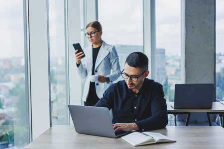 A businessman is working on a laptop while talking while his colleague is listening. Work in a modern bright officeの写真素材