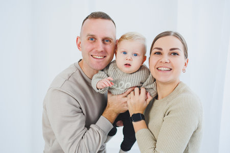 Young family mom and dad with a little six-month-old son on a white background. A married couple hugs their little son. Family relationshipsの写真素材