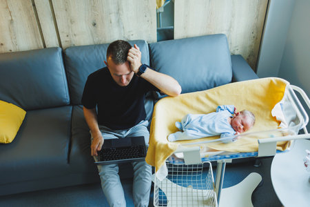 Loving young dad working on laptop and sitting next to baby. Working at home with a small childの写真素材