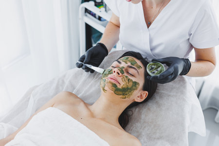 A cosmetologist applies a medical mask to the skin of a woman lying on a couch. Facial. Facial skin care procedure. Moisturizing the face. Face maskの写真素材